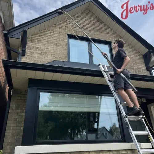 A crew member on a ladder scrubbing the fascia with a long pole