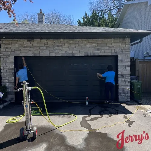 Two crew members washing a garage door with a water-fed pole