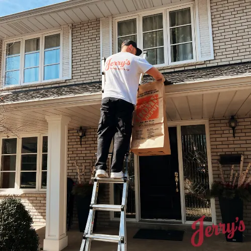 A crew member on a ladder at the roofline with a debris bag, clearing an eavestrough