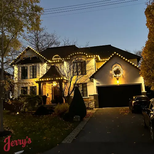 A finished Christmas light install at dusk: roofline, windows and a wreath lit on a two-storey house