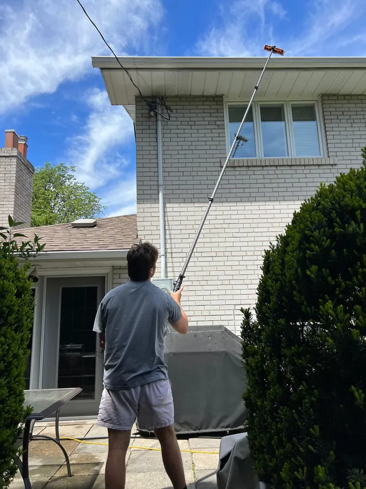 A crew member washing upper windows and siding with a water-fed pole